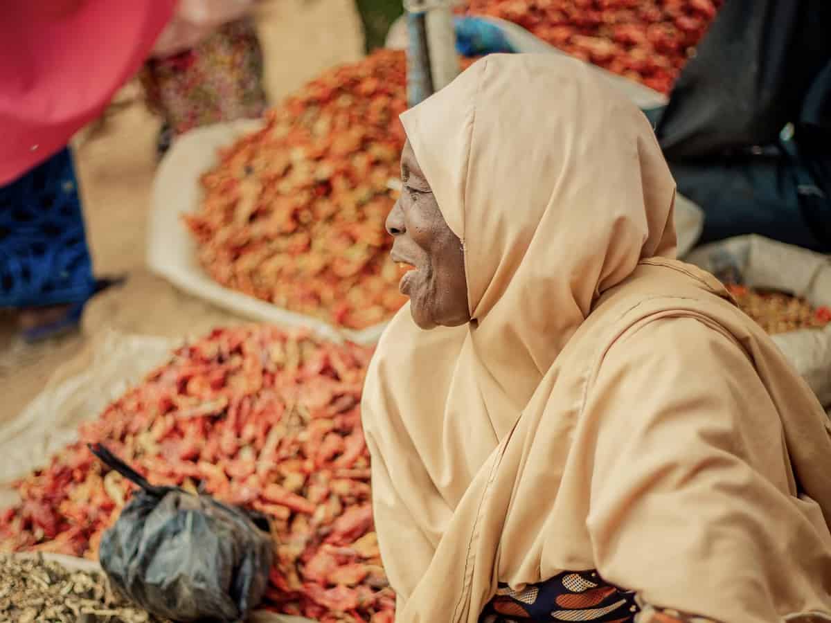 Eine Händlerin mit beigem Kopftuch sitzt neben Haufen getrockneter roter Chilis auf dem Darajani-Markt.
