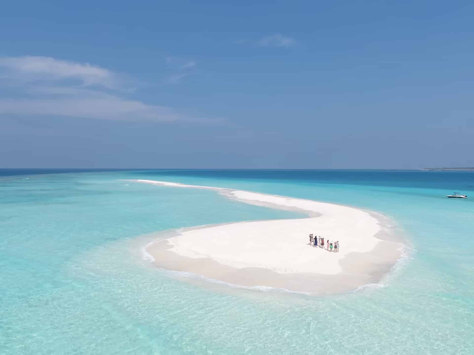 Eine kleine Gruppe Menschen auf der geschwungenen weißen Sandbank von Nakupenda, umgeben von klarem, türkisfarbenem Flachwasser.